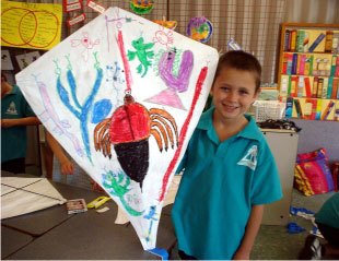 young school boy showing off the make-it-yourself kite he has decorated