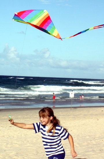 7 year old girl flying rainbow diamond kite on the beach