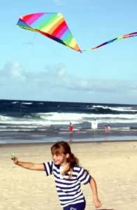 young girl running along the beach flying a rainbow diamond kite from leading edge kites